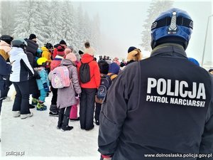policjant z patrolu narciarskiego stojący przy grupie osób na stoku