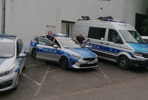 policjant i policjantka stojący przy radiowozie, obok inne zaparkowane radiowozy
