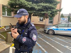policjant trzymający w ręce krótkofalówkę, w tle policyjny radiowóz
