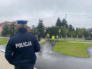 uczeń jadący na rowerze przez miasteczko rowerowe, w pobliżu policjanci oceniający przejazd
