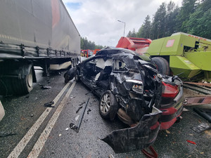 zmiażdżony czarny samochód pomiędzy ciężarówką a maszynami rolniczymi