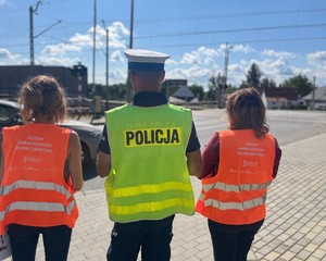 organizatorzy akcji z policjantem stojący tyłem przy przejeździe kolejowym