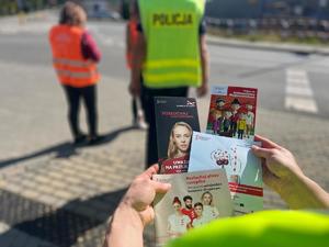 ulotki z akcji bezpieczny przejazd, w tle policjant i organizatorzy