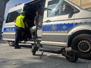policjant stojący przy radiowozie, w radiowozie osoba kontrolowana