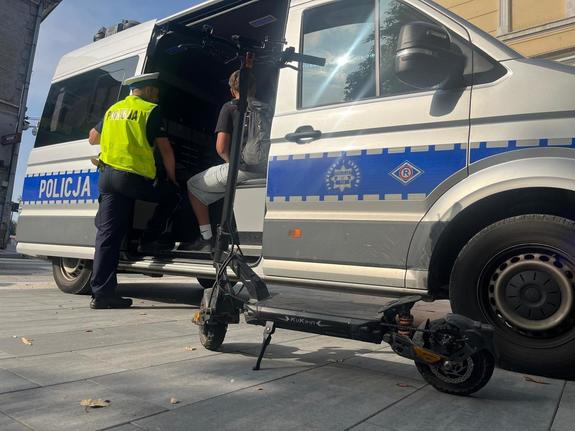 policjant stojący przy radiowozie, w radiowozie osoba kontrolowana