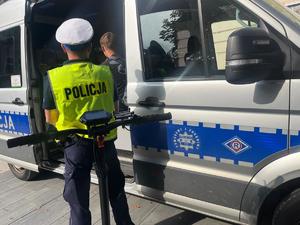 użytkownik hulajnogi elektrycznej siedzący w radiowozie, obok stoi policjant