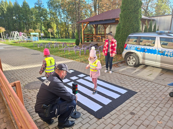 dziecko przechodzące przez przejście dla pieszych, obok policjant przy atrapie sygnalizacji świetlnej