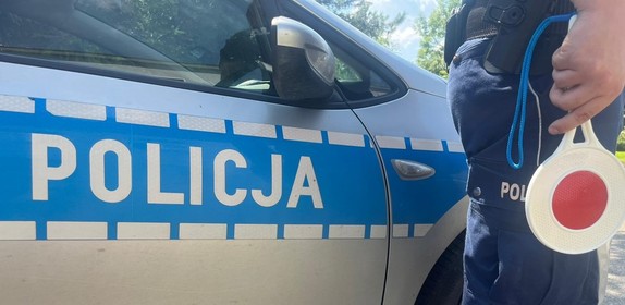 policjant trzymający tarczę do zatrzymywania na tle radiowozu