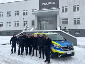 wspólne zdjęcie przedstawicieli władz samorządowych z policjantami na tle radiowozu i komendy