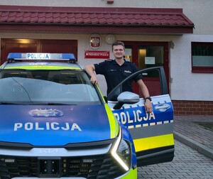 policjant z Czchowa stojący przy radiowozie, w tle komisariat policji w Czchowie