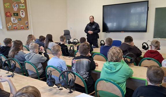 policjant przemawiający do grupy siedzących uczniów