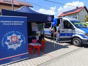 policjantka rozmawiająca z dzieckiem w namiocie profilaktycznym obok osoby oglądające policyjny radiowóz