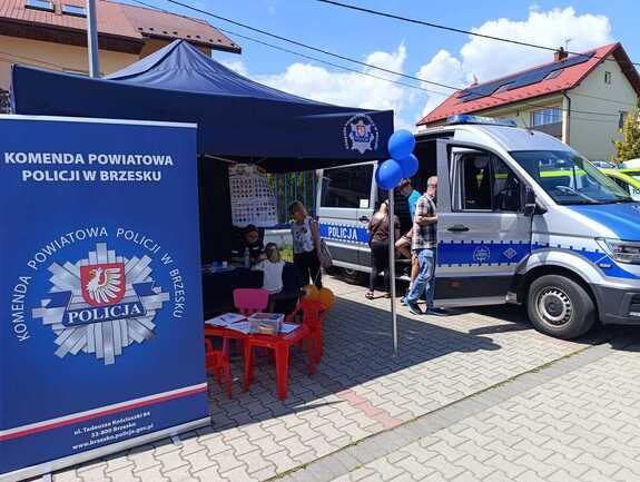 policjantka rozmawiająca z dzieckiem w namiocie profilaktycznym obok osoby oglądające policyjny radiowóz