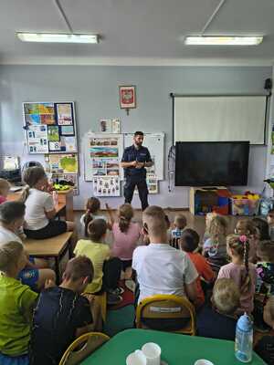 policjant stojący przed grupą dzieci na prelekcji profilaktycznej