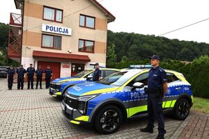 policjanci stojący przy radiowozach, w tle funkcjonariusze tamtejszego komisariatu policji