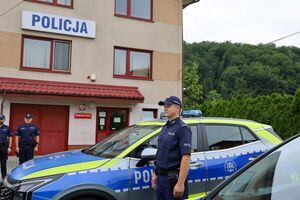 policjant stojący przy radiowozie, w tle budynek komisariatu policji