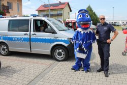 policjant z gryfem, za nimi policyjny radiowóz