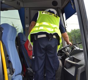 Umundurowany funkcjonariusz Policji stoi wewnątrz autobusu obok kontrolowanego kierowcy