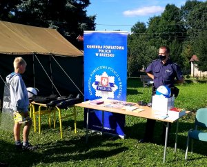 policjant rozmawiajacy z dzieckiem, w tle baner KPP w Brzesku