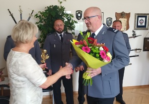 Komendant Powiatowy Policji w Brzesku wręczający kwiaty odchodzącej na emeryturę sekretarce