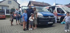 Policjant wraz z grupa osób stoi przy radiowozie policyjnym