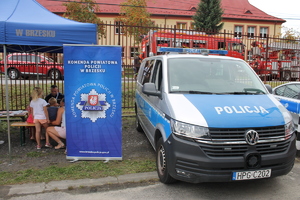 radiowóz policyjny stojący obok namiotu profilaktycznego w którym siedzi policjant opowiadający siedzącym dzieciom o bezpieczeństwie, w tle wozy strażackie