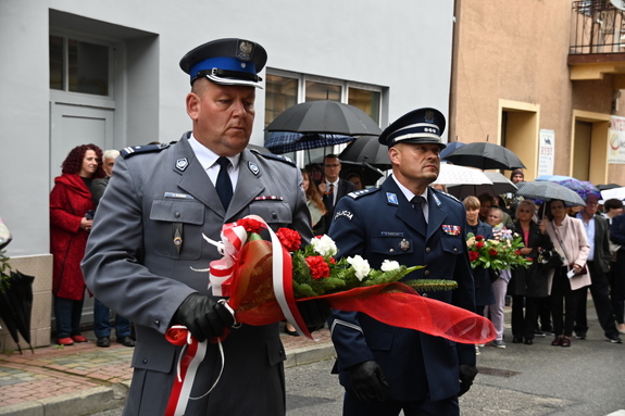 Komendant Powiatowy Policji w Brzesku z Naczelnikiem Wydziału Prewencji  z wiązanką biało-czerwonych kwiatów przed tablicą upamiętniającą ofiary holokaustu