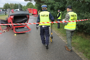 policjant mierzący wózkiem odległości w pobliżu samochodu leżącego na dachu