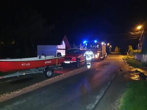 wozy strażackie i łódź motorowa stojące przy drodze, drogą idący strażak