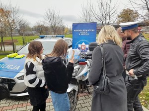 policjant wraz z uczestnikami pikniki stojący przy policyjnym motocyklu, w tle radiowóz i baner Komendy Powiatowej Policji w Brzesku