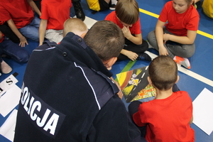policjant przyglądający się rysunkowi złożonemu z puzzli przez czteroosobową drużynę dzieci