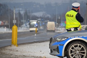 Policjant ruchu drogowego stoi przy zaparkowanym radiowozie, mierzy prędkość