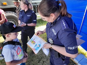 policjantka pokazująca materiały profilaktyczne o bezpieczeństwie nad wodą chłopcu, w tle druga policjantka