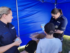 policjantka wręczająca nagrodę w formie płyty cd chłopcu, który brał udział w konkursie profilaktycznym, obok druga policjantka