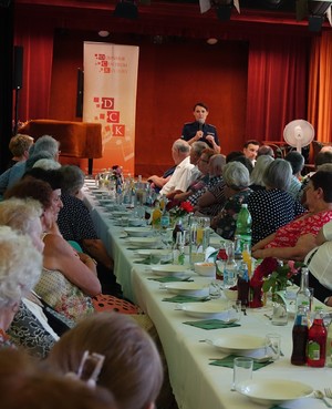 policjantka przemawiająca do grupy seniorów siedzących przy stole