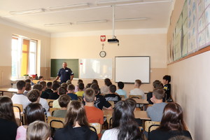 policjant przemawiający do grupy uczniów siedzących przy klasowych ławkach