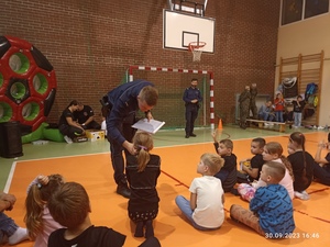 policjant trzymający przy ustach odopowiadającej dziewczynki mikrofon