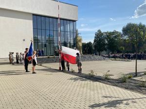 grupa harcerzy trzymająca wciąganą na maszt flagę Polski