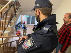 stojący przy schodach policjant, w tle strażacy w holu Starostwa Brzeskiego