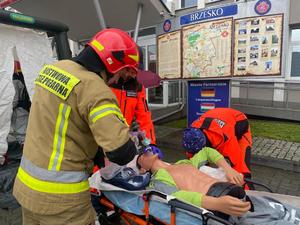 ratownicy medyczni i strażak udzielający pierwszej pomocy poszkodowanemu leżącemu na noszach