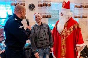 komendant powiatowy policji w Brzesku trzymający mikrofon w ręce i rozmawiający z podopiecznym domu pomocy społecznej, obok stoi mikołaj